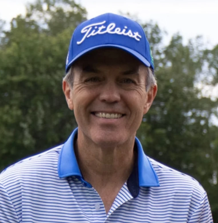 Tom Caron, smiling in a blue golf cap and striped polo